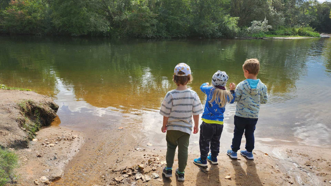 Drei Kinder stehen am Flussrand und beobachten die Natur.