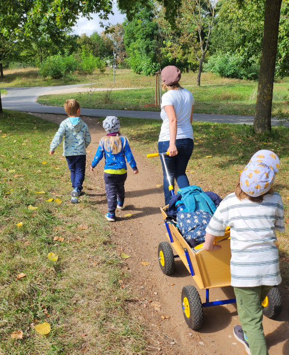 Eine Museumspädagogin läuft mit drei Kindern und einem Bollerwagen durch den Wiesengrund.