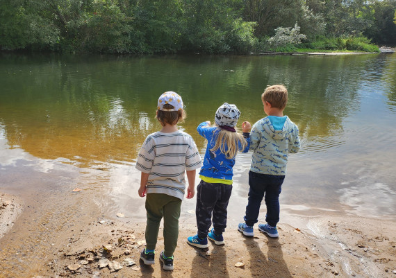 Drei Kinder stehen am Flussrand und beobachten die Natur.