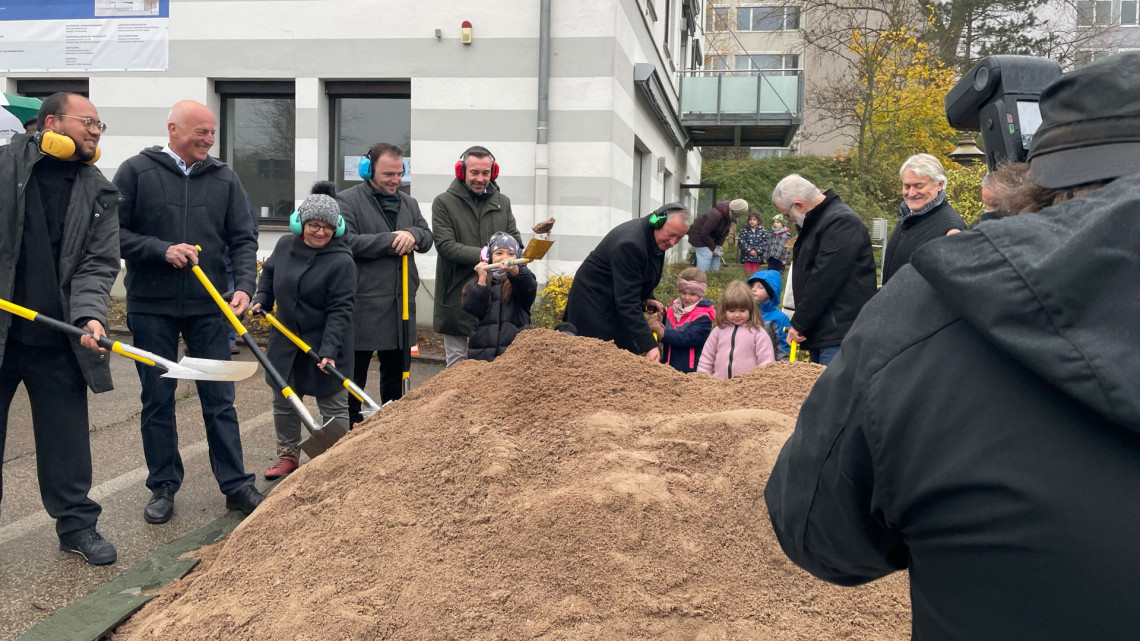 Geladene Gäste und Kinder mit Schaufeln am symbolischen Sandhaufen für den Spatenstich.