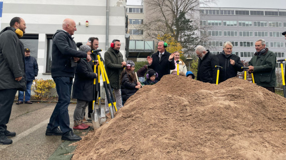 Stadtprominenz mit Schaufeln vor einem Sandhaufen anlässlich des Spatenstichs.